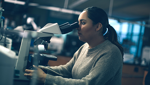 A young woman looking through a microscope in a lab