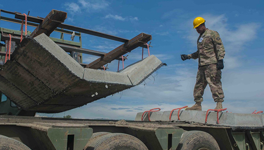 A Military service member standing atop a flatbed trailer at a construftion site