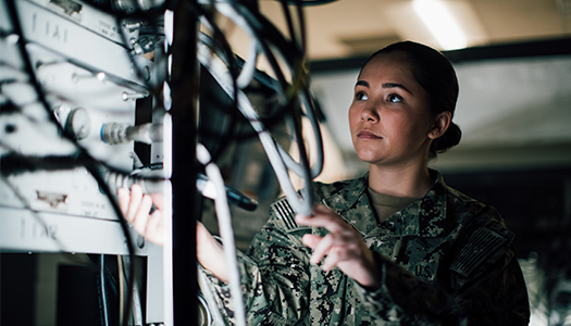 A US Navy service members examines a series of cables behind computer servers.