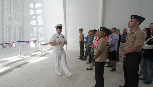 A Navy service member with a large group gathered inside a memorial area