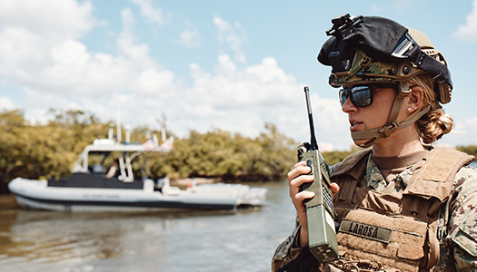 A US Navy service member standing in a boat communicating on a radio