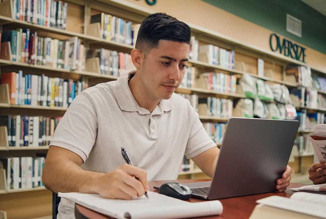 A student taking notes while simultaneously working on his laptop