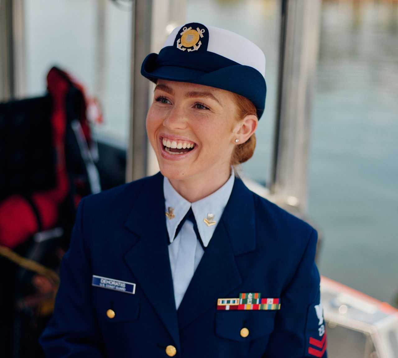 A woman in uniform smiles while standing on a boat