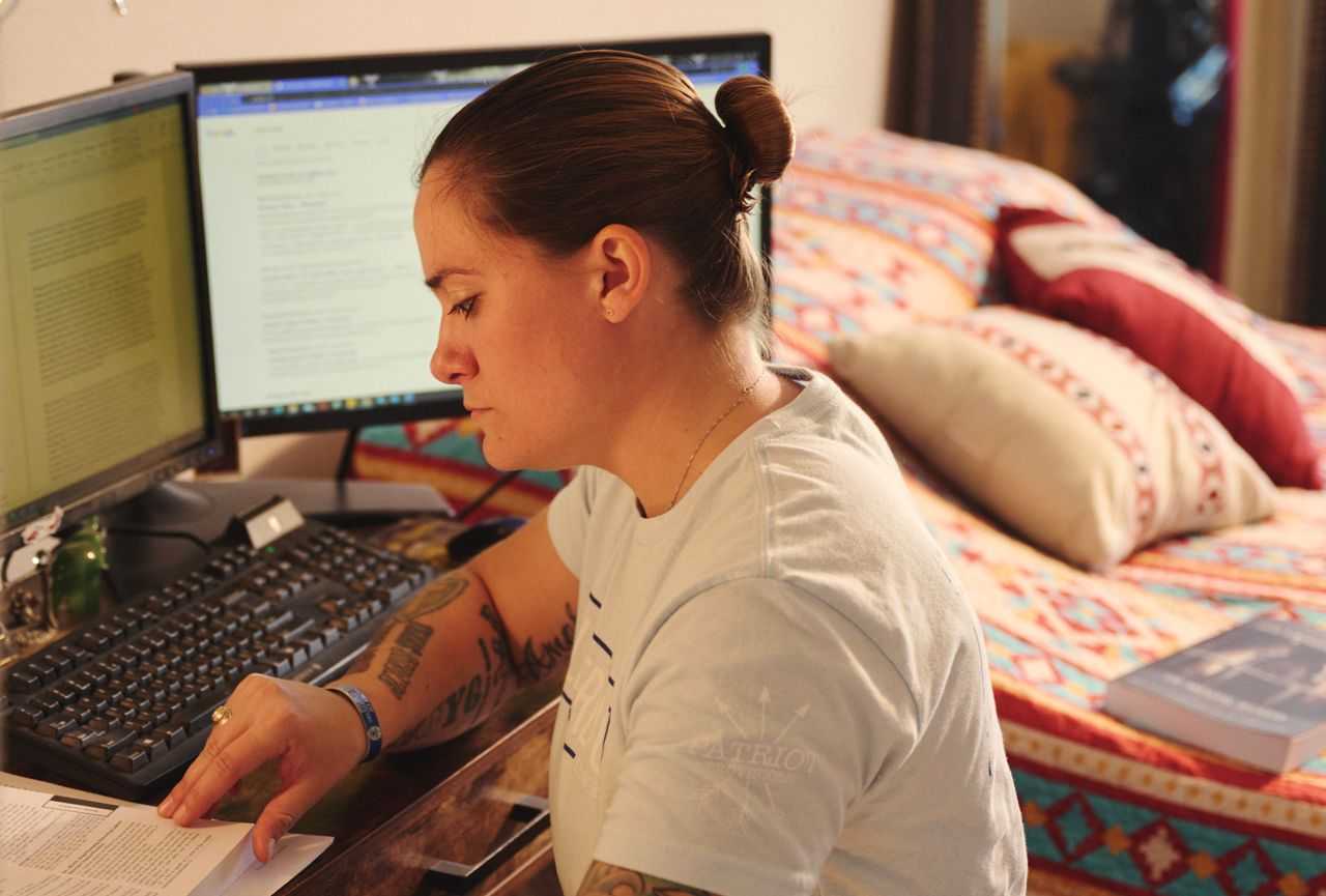 A student sits in front of multiple computer screens while reviewing some papers