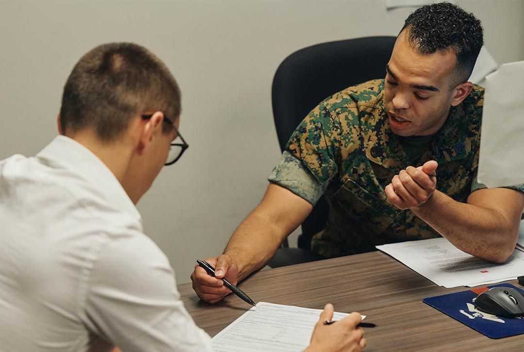Man in uniform explaining a document to another man seated at a desk