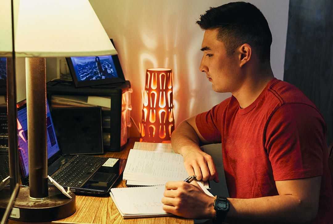 A student takes notes while reading something off his laptop