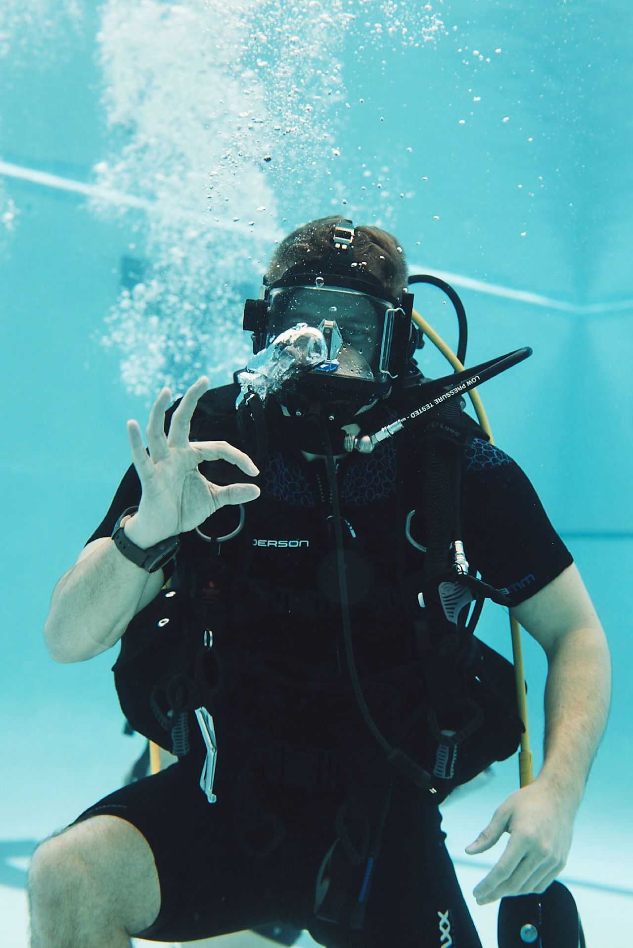 A diver in a scuba suit giving the "OK" sign while underwater